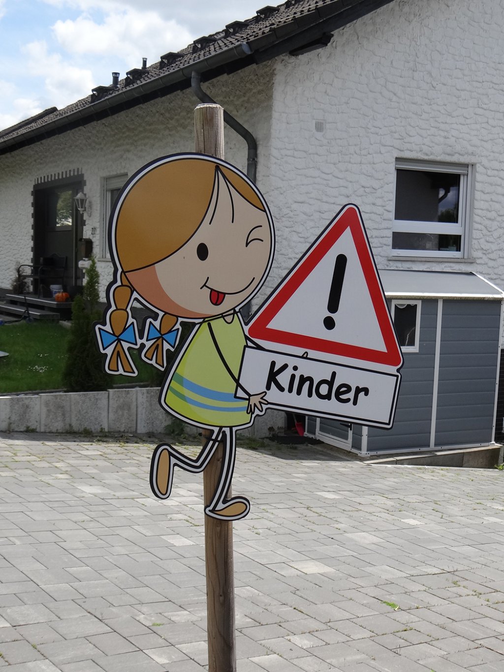 Foto eines Schildes eines zwinkernden Mädchens mit Verkehrszeichen Achtung Kinder in der Hand.